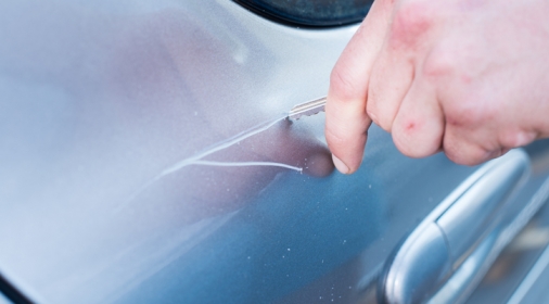 Man's hand scratching a car with a key.